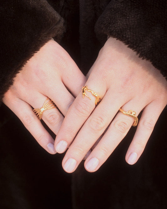 hands wearing gold rings including the Sisyphus Ring