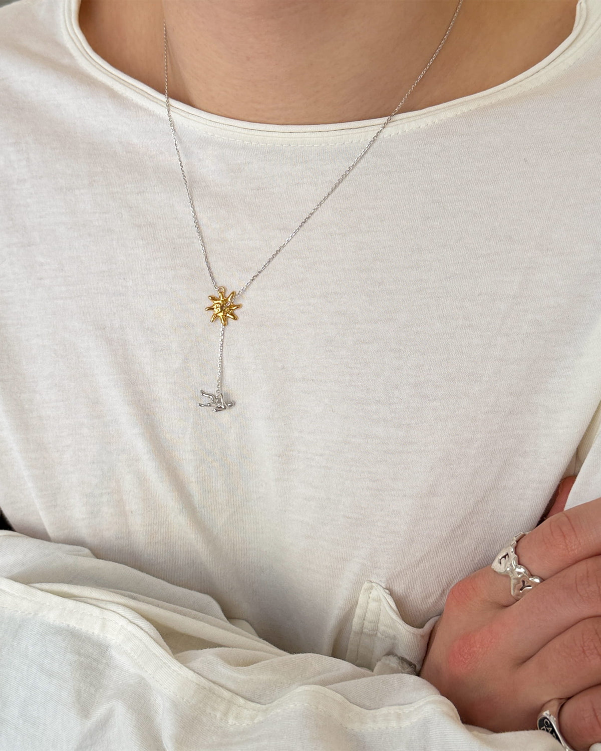 Icarus Necklace in silver with a gold sun worn by a male in a white long sleeve