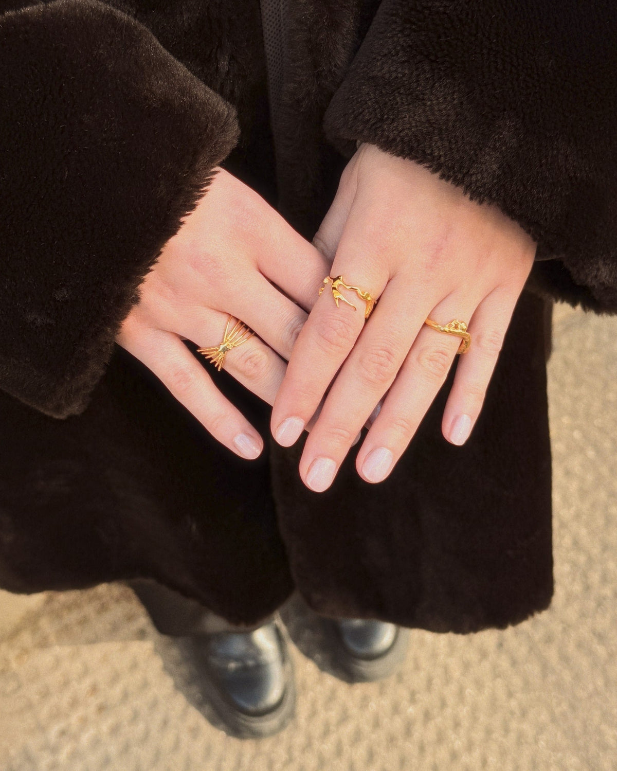 person in winter coat showing gold rings including the Sisyphus Ring